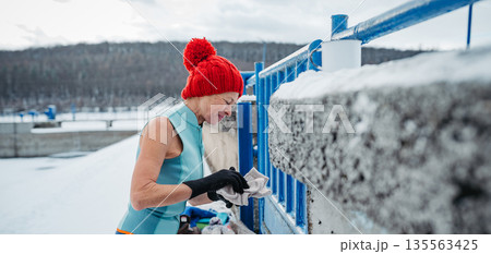 Senior woman preparing for winter swimming in an icy lake for health benefits. Senior woman preparing for winter swimming in an icy lake for health benefits. 135563425