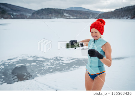 Older woman enyoing hot tea after ice bathing in lake. Older woman enyoing hot tea after ice bathing in lake. 135563426