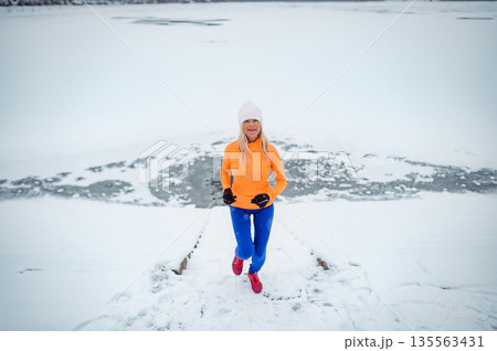 Active elderly woman jogging in cold snowy weather. 135563431