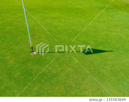 Golf hole with a flag on a lush green putting green during a bright sunny day. Golf hole with a flag on a lush green putting green during a bright sunny day. 135563694