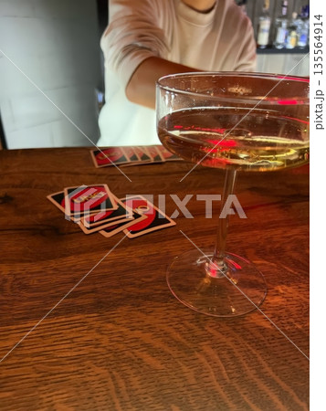 A stylish cocktail glass sits on a wooden bar, with colorful UNO cards in the foreground. A hand reaches out, enhancing the playful ambiance of the evening. 135564914