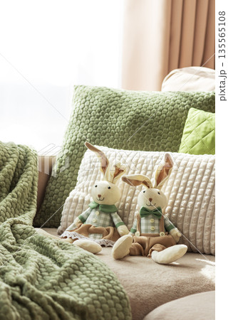 Cozy Sofa with Plush Easter Bunny Dolls and Textured Pillows in Sunlight Cozy Sofa with Plush Easter Bunny Dolls and Textured Pillows in Sunlight 135565108