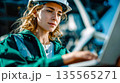 Female engineer wearing safety helmet and reflective jacket working on laptop at industrial facility or construction site 135565271