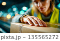 Female warehouse worker sealing cardboard box with tape during logistics and packaging process in distribution center 135565272