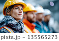 Confident team of industrial workers wearing safety helmets and protective clothing, standing together with crossed arms in a studio setting 135565273