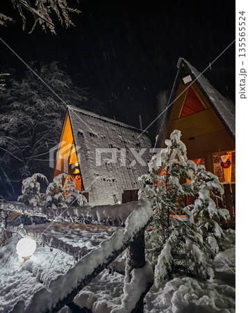 Two Wooden A Frame Cabins Surrounded by Snowy Fir Trees at Night Two Wooden A Frame Cabins Surrounded by Snowy Fir Trees at Night 135565524