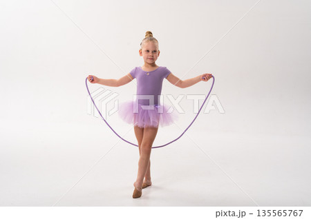 Young ballerina with a cochlear implant stretches a red hoop while posing in a lavender tutu. Inclusive gymnastics, hearing technology, and childhood coordination through rhythmic dance and movement. 135565767