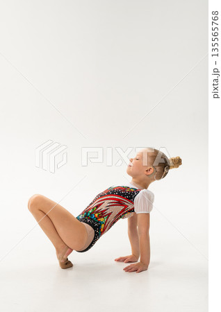 Young rhythmic gymnast with cochlear implant posing in training leotard in studio. Hearing rehabilitation, inclusive childhood sport and body awareness through flexibility and balance 135565768