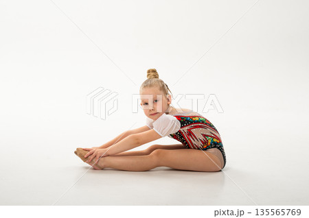 Side view of gymnast with cochlear implant stretching in studio leotard. Hearing rehabilitation, posture control and inclusive childhood physical development through rhythmic training 135565769