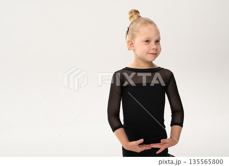 Little girl in black latin dance dress performing graceful pose with cochlear implant. Copy space. Overcoming hearing loss through movement, inclusion, and confidence in art and rhythmic self 135565800