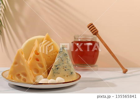 Assortment of different types of cheese: blue cheese, gorgonzola, roquefort, parmesan, mozzarella, maasdam with honey on the kitchen table, a selection of healthy and natural products 135565841