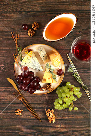 Still life with gourmet blue cheese, parmesan, grapes, honey, nuts, rosemary and wine. Top view of cheese plate with seasonal wine appetizers, Italian cuisine concept, restaurant and cafe menu. Still life with gourmet blue cheese, parmesan, grapes, honey, nuts, rosemary and wine. Top view of cheese plate with seasonal wine appetizers, Italian cuisine concept, restaurant and cafe menu. 135565847