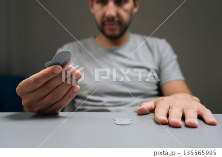 Man holding adhesive game thumb pad, ready to apply to smartphone screen for improved control and more comfortable mobile gaming experience, demonstrating gaming accessories. Man holding adhesive game thumb pad, ready to apply to smartphone screen for improved control and more comfortable mobile gaming experience, demonstrating gaming accessories. 135565995