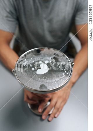 Vertical close-up view of man cleaning small dirty mirror with soap suds, heart print visible in foam, representing , love for hygiene, dedication to keeping domestic space tidy and clean. Vertical close-up view of man cleaning small dirty mirror with soap suds, heart print visible in foam, representing , love for hygiene, dedication to keeping domestic space tidy and clean. 135565997