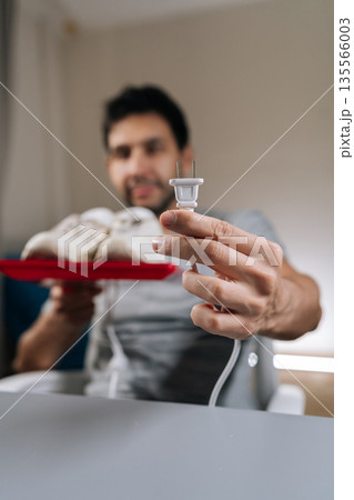 Vertical focus on foreground of blurred male holding electric plug for shoe dryer, preparing to clean and dry white sneakers, focusing on home care routine and footwear maintenance. Vertical focus on foreground of blurred male holding electric plug for shoe dryer, preparing to clean and dry white sneakers, focusing on home care routine and footwear maintenance. 135566003