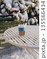 Hot takeaway coffee on a snowy outdoor table in winter park. Cozy winter morning concept, warm drink during cold weather, minimal lifestyle scene with copy space. Cafe or coffee shop terrace No people 135566434