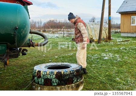 Sanitation worker operating sewage vacuum truck hose near rural cesspit emptier opening during routine waste removal process at homestead. Sanitation worker operating sewage vacuum truck hose near rural cesspit emptier opening during routine waste removal process at homestead. 135567041