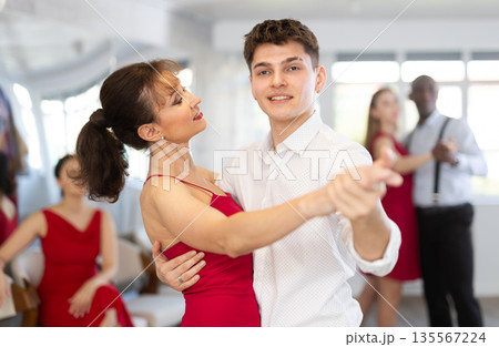 Young guy and woman in red dress waltzing during group class 135567224