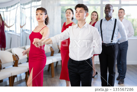 Young guy and woman in red dress waltzing during group class 135567286