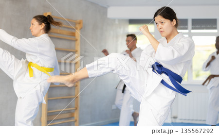 Middle-aged woman attendee of karate classes practicing kata standing in row with others 135567292