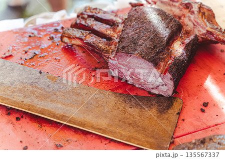 Cooked meat on a red cutting board with a wooden carving knife resting beside it, showcasing a well-seasoned crust and juicy interior during a barbecue preparation Cooked meat on a red cutting board with a wooden carving knife resting beside it, showcasing a well-seasoned crust and juicy interior during a barbecue preparation 135567337