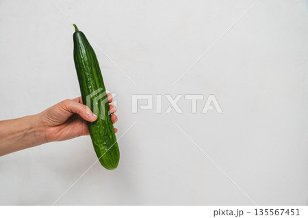 Hand holding a fresh green cucumber against a plain white background with ample copy space for text or design elements in a minimalistic style 135567451