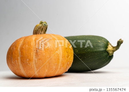 Orange pumpkin and green zucchini placed on a light surface with a soft gradient background, showcasing their natural textures and colors for culinary or seasonal use Orange pumpkin and green zucchini placed on a light surface with a soft gradient background, showcasing their natural textures and colors for culinary or seasonal use 135567474
