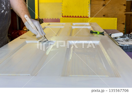 Painter uses brush to paint door while tools paint supplies are on nearby table Painter uses brush to paint door while tools paint supplies are on nearby table 135567706