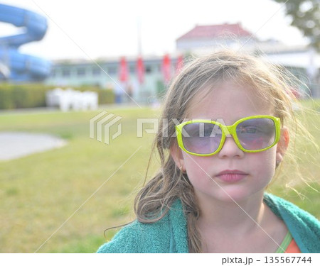 A sweet little girl wearing sunglasses at the pool. A smiling little girl wearing a beach towel at the pool. Happy kid at aqua. Little girl in sunglasses on a summer sunny day. Summer holiday concept A sweet little girl wearing sunglasses at the pool. A smiling little girl wearing a beach towel at the pool. Happy kid at aqua. Little girl in sunglasses on a summer sunny day. Summer holiday concept 135567744