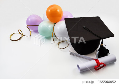 Graduation cap with diploma, books, and celebration balloons 135568052