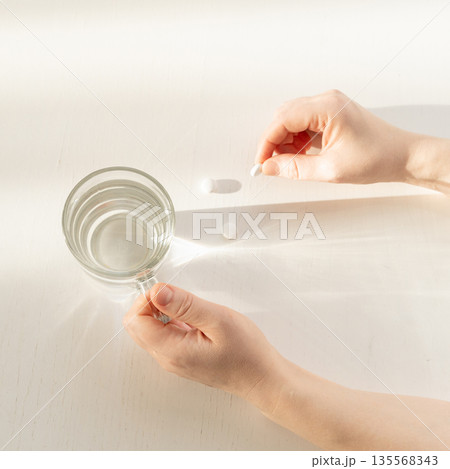 Person taking medication with glass of water Person taking medication with glass of water 135568343