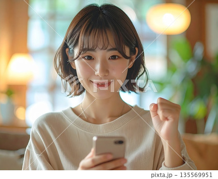 スマートフォンで成功や合格を確認しガッツポーズする若い女性：プレゼン資料やWebデザイン用人物素材 135569951