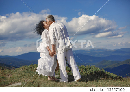 Senior man and woman in the mountains. Adult couple in love at sunset. Man in a white shirt. 135571094
