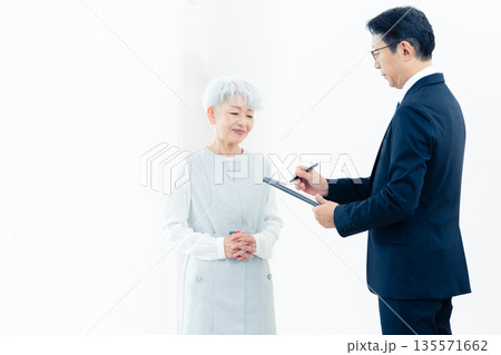 営業マンの説明を聞くシニア女性 135571662