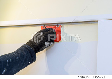 Worker applies paint with tool on wall in home renovation project in room 135572158
