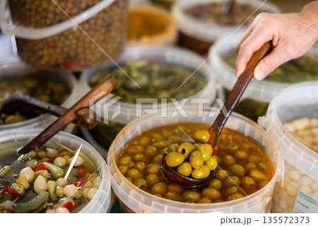 Hand using ladle takes out handful of salted olives from bucket. Hand using ladle takes out handful of salted olives from bucket. 135572373