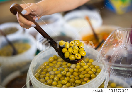 Hand scoops green pitted olives from buckets Hand scoops green pitted olives from buckets 135572395