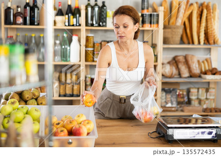 Adult woman seller weighs apples in bag Adult woman seller weighs apples in bag 135572435