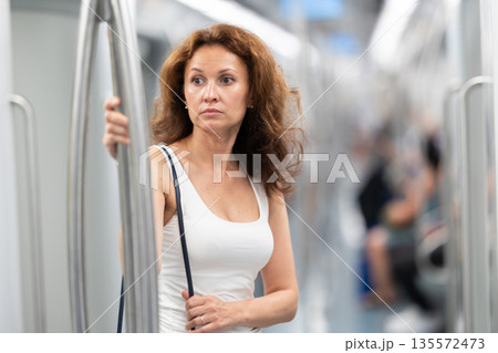 Adult woman stands in subway car Adult woman stands in subway car 135572473