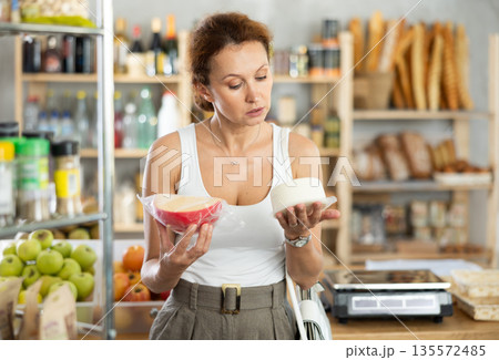 Woman carefully chooses delicious cheese in grocery department of supermarket 135572485