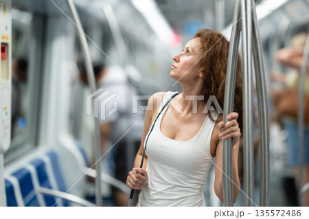 Adult woman stands in subway car Adult woman stands in subway car 135572486