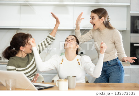 Three happy middle-aged woman expressing joy for winning in the kitchen Three happy middle-aged woman expressing joy for winning in the kitchen 135572535
