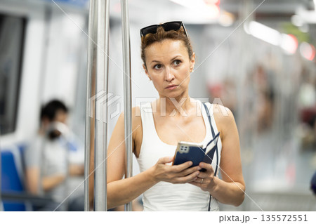 Adult woman standing in subway car with phone Adult woman standing in subway car with phone 135572551