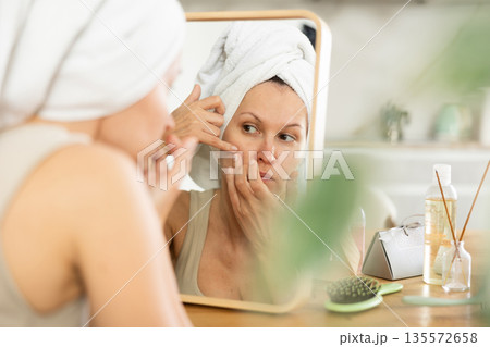 Middle-aged woman examining her facial skin looking in the mirror put on the table 135572658