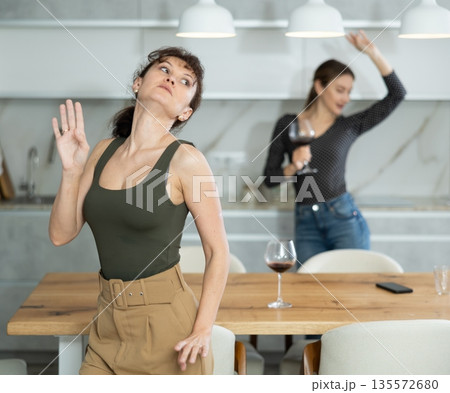Middle-aged women dancing at the kitchen-table with wineglasses Middle-aged women dancing at the kitchen-table with wineglasses 135572680