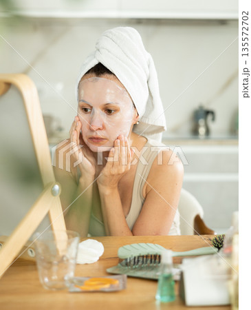 Woman in towel turban on head applying hydrating face mask 135572702