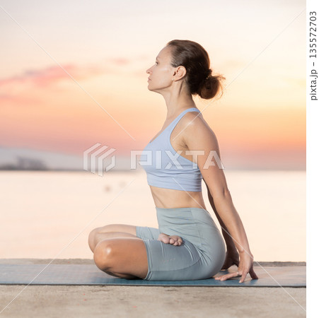 Near sea during sunset, girl performs variations of padmasana 135572703