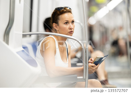 Adult woman sitting in subway car with phone 135572707
