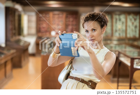Woman takes pictures of exhibits in glass cases at history museum using her smartphone 135572751