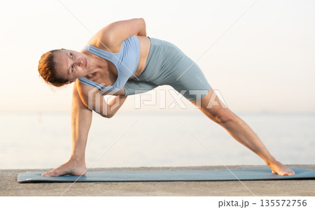 Near sea during sunset, girl performs Parivritta Parshvakonasana Near sea during sunset, girl performs Parivritta Parshvakonasana 135572756